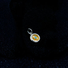 Round gold and silver pendant with blue gem on black velvet background
