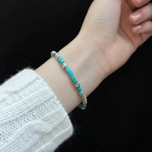 Close-up of wrist wearing a delicate turquoise and silver beaded bracelet against black background